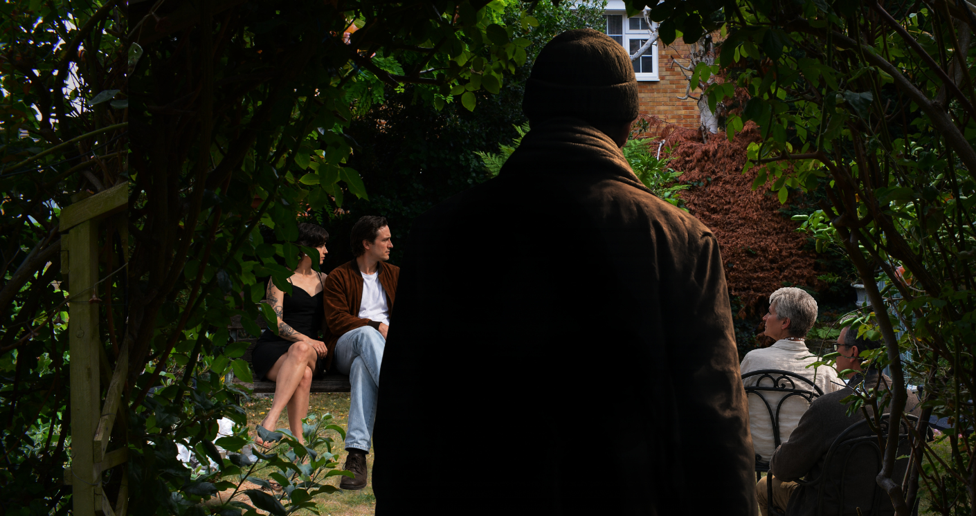 A figure with his back to the camera watches two couples, one older and one younger, from the bushes.